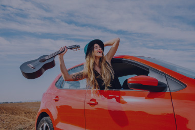 Woman leaning out of car window with a guitar.