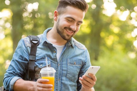 Man outside looking at smartphone holding drink.